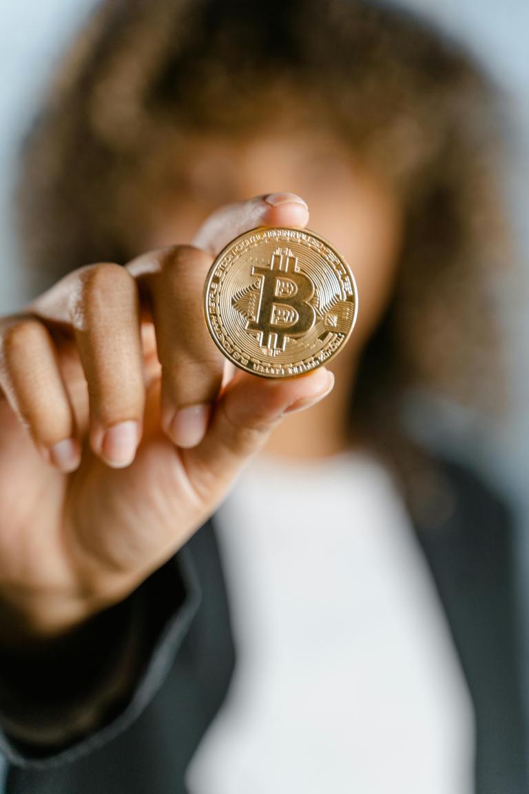 A woman holds a golden Bitcoin coin with a blurred background, emphasizing cryptocurrency.